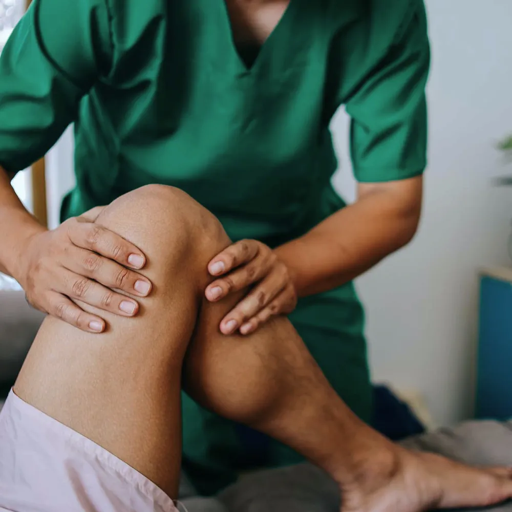 kinésithérapeute-ostéopathe, expert en reprogrammation neuromusculaire en action, manipulant un genou d'un patient à Dax et Bayonne